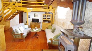 A cozy, rustic living room with wooden beams, a sofa, a television, and a wood-burning stove. - Holiday Villa in Village Rakalj (Marcana)