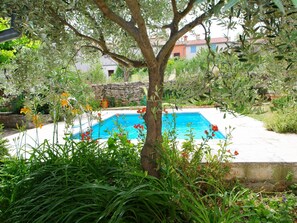 A swimming pool surrounded by lush greenery and a stone wall. - Holiday Villa in Village Rakalj (Marcana)