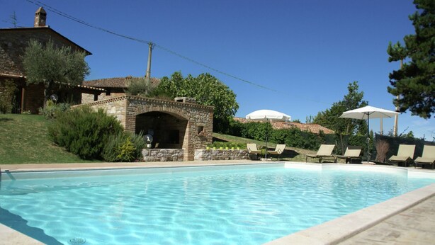 A swimming pool with lounge chairs and umbrellas, surrounded by stone buildings and greenery. - Villa in Umbertide With Pool and Garden (Umbertide)
