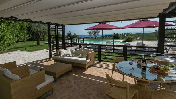 An outdoor patio with wicker furniture, a glass table with wine glasses and fruit, and a view of a pool and mountains. - Farmhouse in Montoro Near Montoro Castle (Narni)