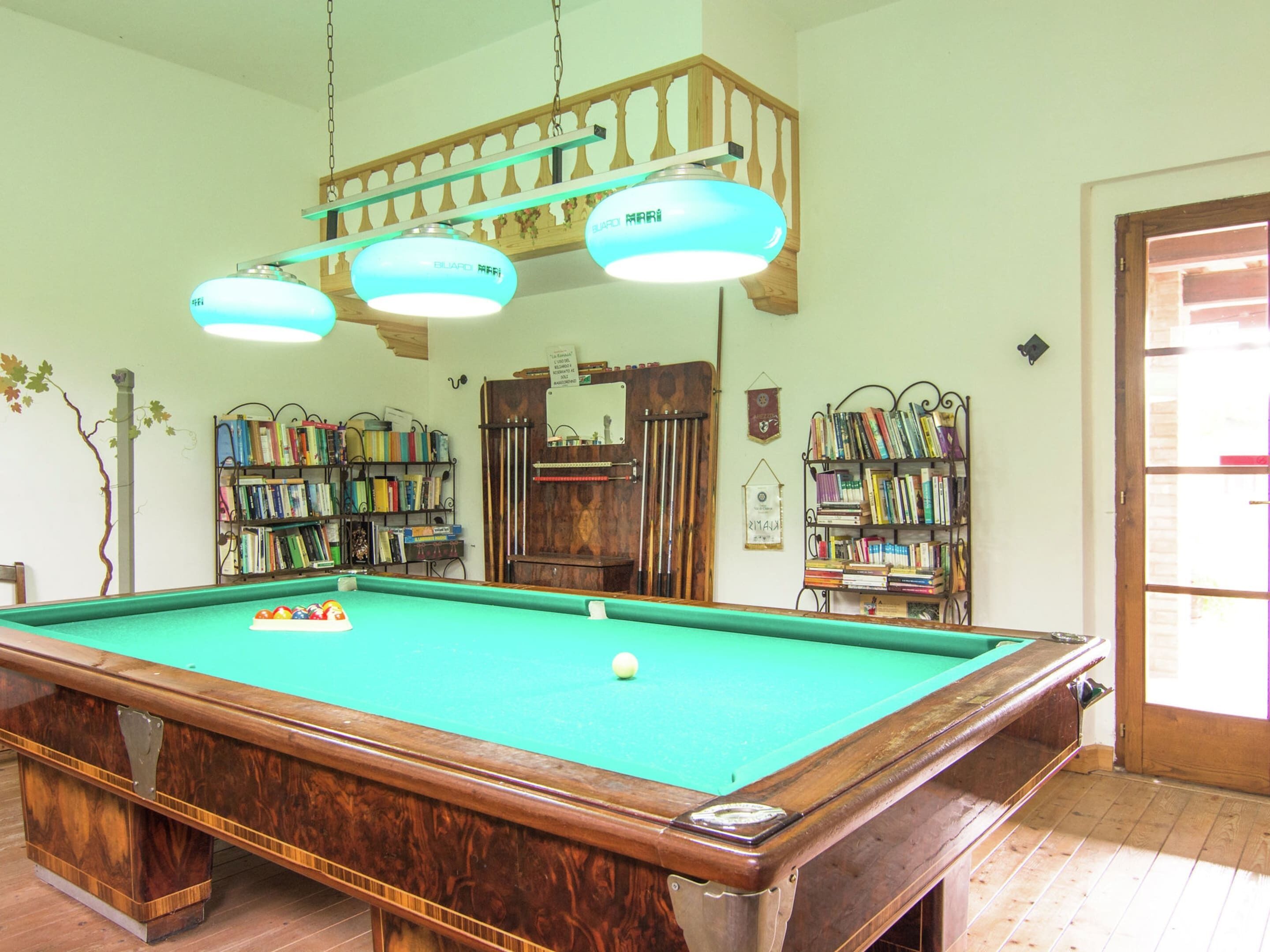 Een pooltafel met houten afwerking, omringd door boekenplanken vol boeken, en een houten trap met een leuning.