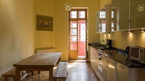 Una cocina con piso de madera, una mesa de madera con bancos, un refrigerador, un microondas y una lámpara colgante.