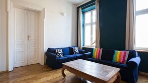 Una sala de estar con una mesa de centro de madera, dos sofás con cojines estampados, un tapete a rayas y un ventanal con cortinas.