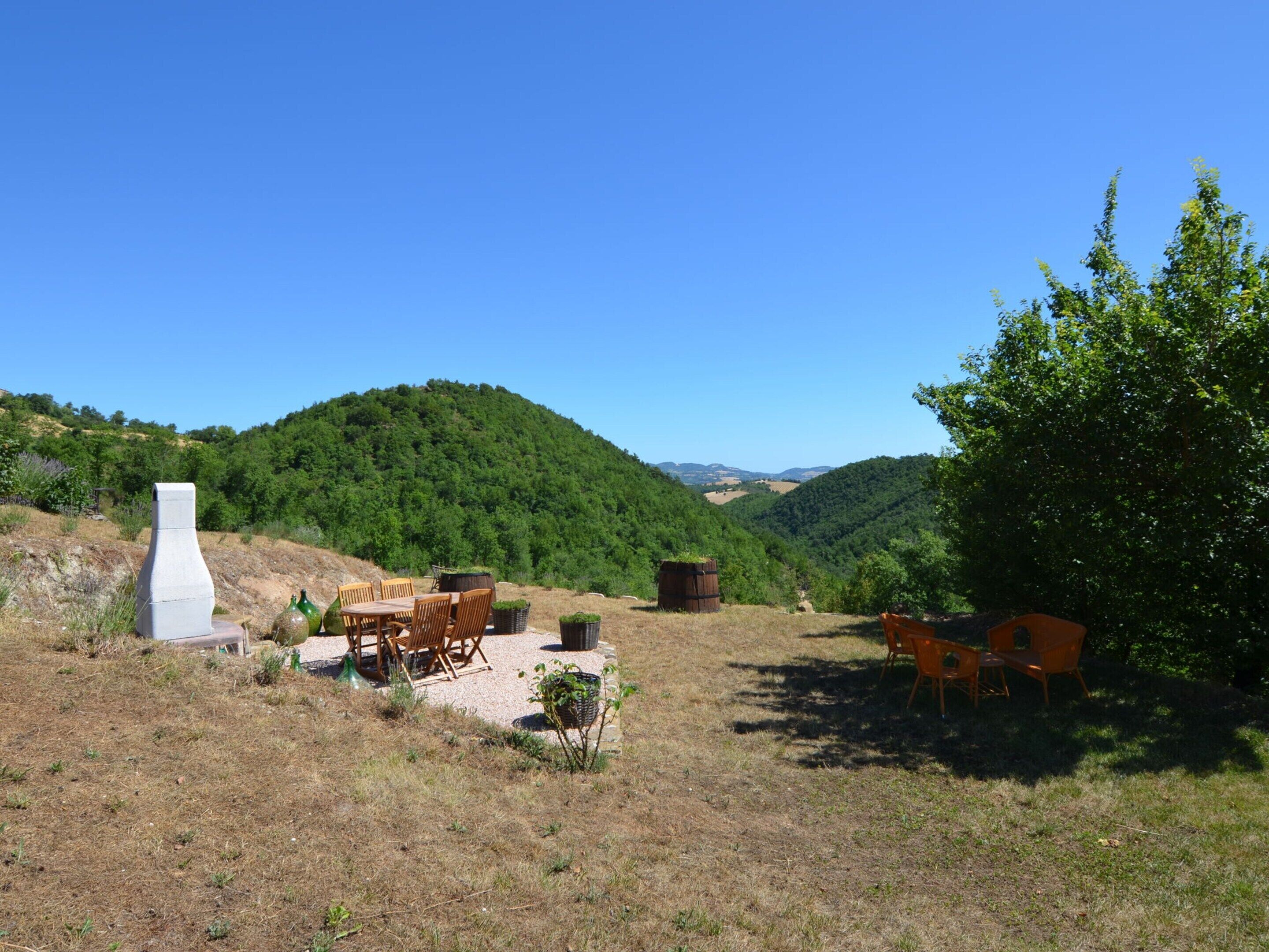 Un espace extérieur aménagé avec une table et des chaises, entouré d’un paysage naturel composé de collines et d’arbres.