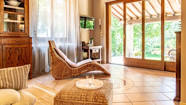 A living room with a wicker chair, a sofa, a wooden cabinet, a television, and a large sliding glass door leading to a garden. - Cottage in Tuscany With Private Pool (Montecatini Terme)