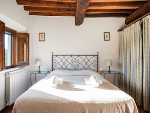 A bedroom with a bed, two bedside tables, a window, and a radiator.