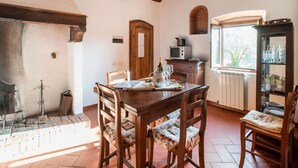 A rustic dining area with a wooden table and chairs, a brick wall, and a window with a view of greenery. - Holiday Home With Vineyard Vibes (San Casciano in Val di Pesa)