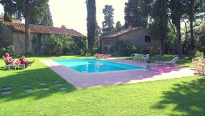 A swimming pool with a tiled deck, surrounded by grass and trees. There are lounge chairs and a table with chairs. - Holiday Home With Vineyard Vibes (San Casciano in Val di Pesa)