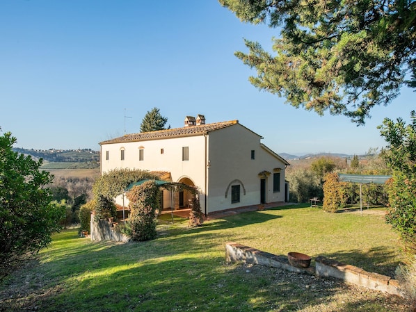 A two-story house with a tiled roof, a small garden, and a view of the countryside.