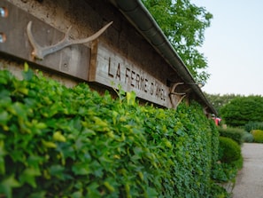 A wooden sign with the text 'LA FERME D'AMEL' partially obscured by foliage.