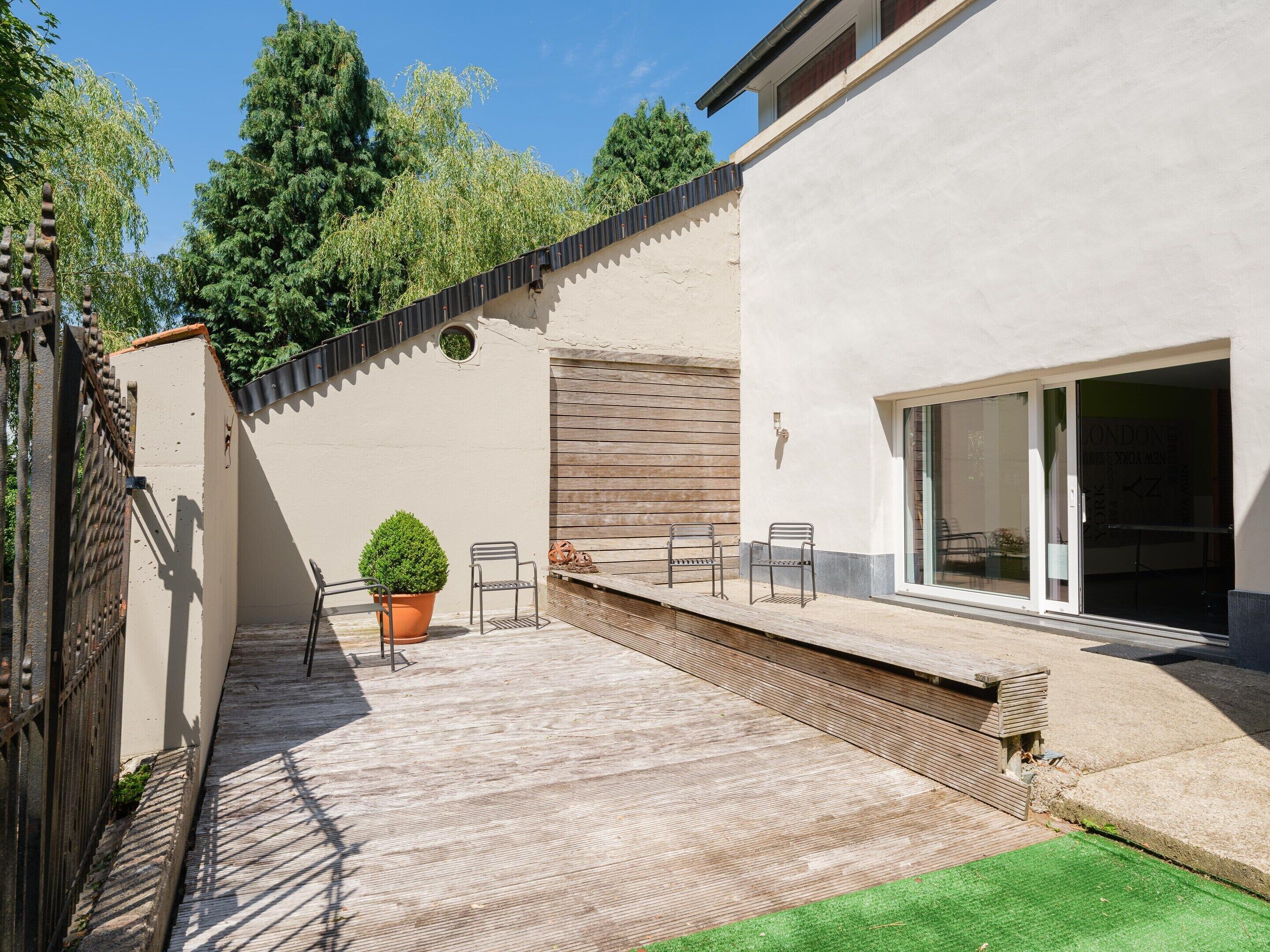 Un patio moderne agrémenté d’une plante en pot, de deux chaises en métal et d’un banc en bois.