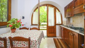 A kitchen with wooden cabinets, a dining table with chairs, a potted plant, and a view through an arched doorway to an outdoor area. - Apartment in Country House near Center of Sorrento (Sorrento)