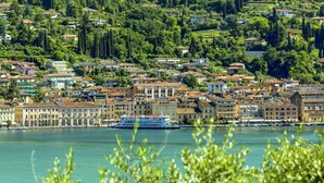 A coastal town with buildings along the waterfront, a large cruise ship docked, and lush greenery in the background. - Belvilla by OYO Trilo Della Cascina (Salò)