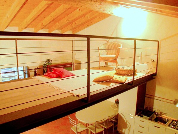 A high-ceilinged room with a bunk bed, a wicker chair, and a small dining table with chairs.