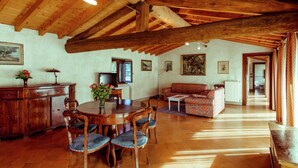 A rustic dining area with a wooden table and chairs, a sofa, and a television in the background. - Belvilla by OYO Trilo Della Cascina (Salò)