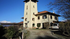 A two-story building with a tower, a covered porch, and a vehicle parked in front. - Farmhouse in Verbania With Mountain Views (Verbania)