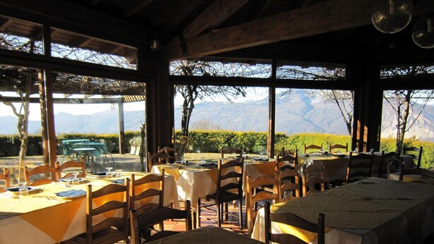 A restaurant with tables set for dining, large windows offering mountain views, and a rustic interior design. - Cottage in Intra With Lake and Mountain Views (Verbania)