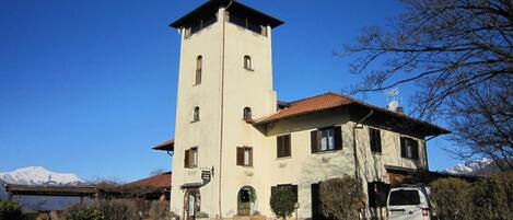 A two-story building with a tower, a covered porch, and a vehicle parked in front.