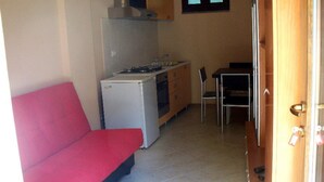 A compact room with a kitchenette, a red sofa, a dining table with chairs, and a wooden door. - Cottage in Intra With Lake and Mountain Views (Verbania)