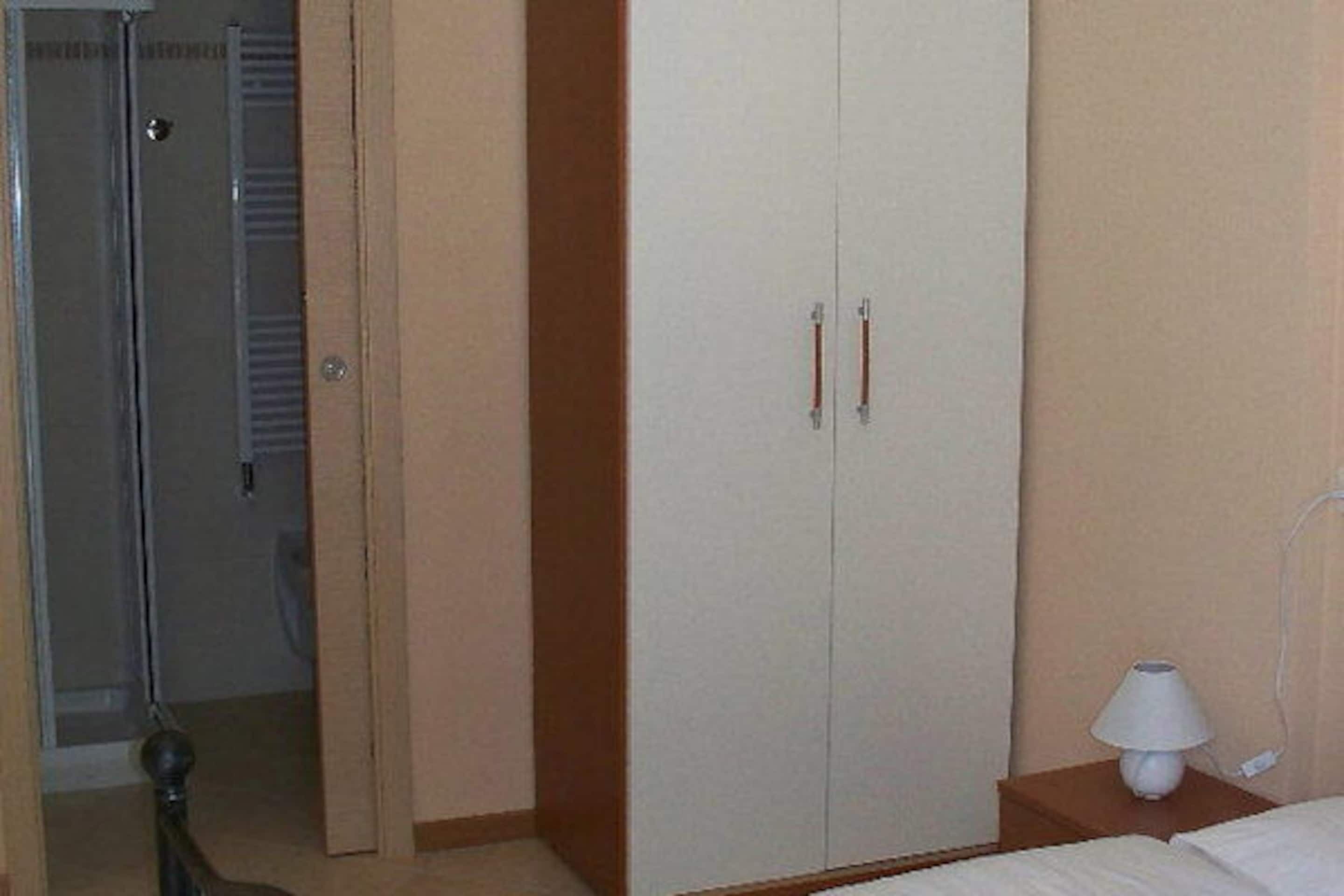A hotel room with a bed, a nightstand with a lamp, a wardrobe, and a door leading to a bathroom.