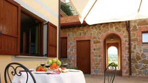 A table set with fruits, wine glasses, and bread, with a stone wall and a view in the background. - Apartment in Monte del Lago Near Lake Trasimeno (Magione)