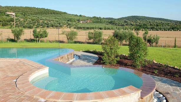 A swimming pool with a curved design, surrounded by a stone deck. - Apartment in Monte del Lago Near Lake Trasimeno (Magione)