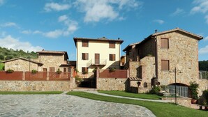 A stone building with a central entrance, surrounded by a paved courtyard and greenery. - Apartment in Monte del Lago Near Lake Trasimeno (Magione)
