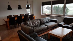 Een moderne woonkamer met een leren bank, een houten salontafel en een eethoek met stoelen en een tafel.