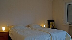 Een slaapkamer met een groot bed, bedlampen, een teddybeer en een raam.
