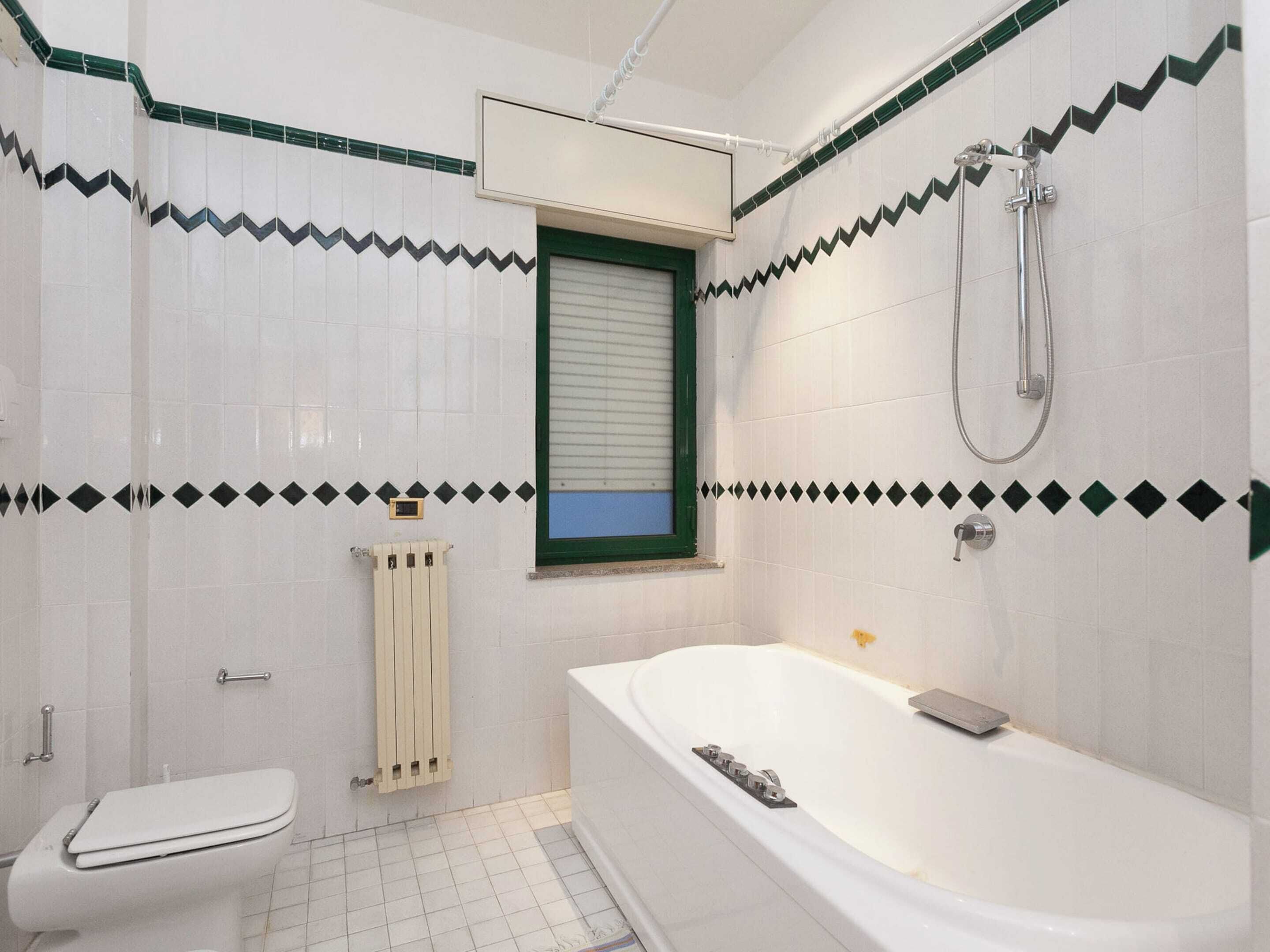 Une salle de bain avec une baignoire, des toilettes et une fenêtre avec des stores.
