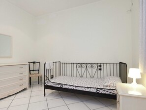 A bedroom with a metal bed frame, a white dresser, a chair, and a bedside table with a lamp. - Belvilla by OYO Vesuvio (Trecase)