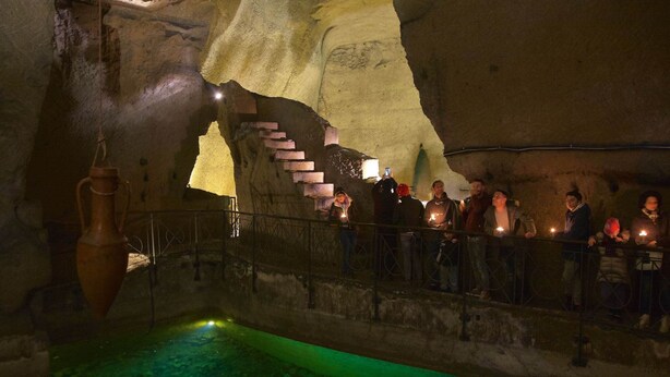 En grotta med en vattenpool inuti, stentrappor och en upphängd vas.