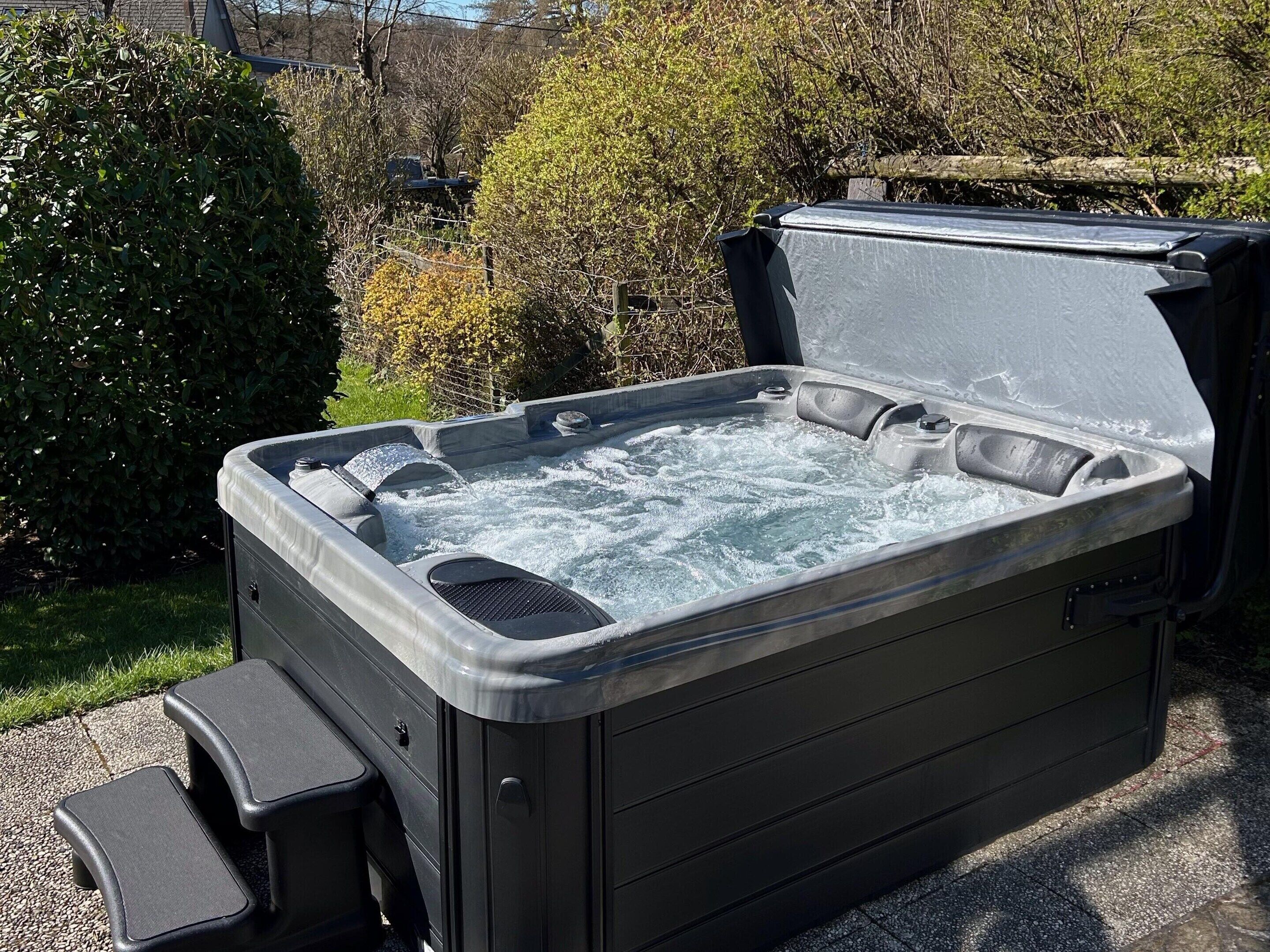 A hot tub with a lid open, surrounded by greenery.