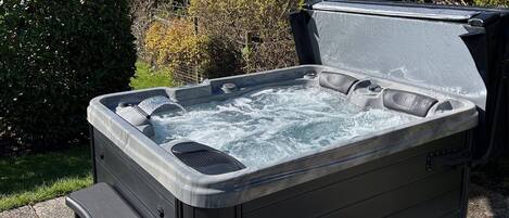 A hot tub with a lid open, surrounded by greenery.