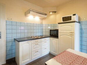 Een keuken met witte kastjes, een zwarte magnetron en een betegelde spatwand.