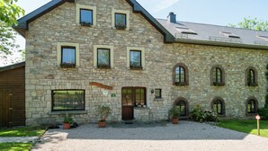 Ein Gebäude aus Stein mit einem Satteldach, zahlreichen Fenstern und einer Schotterauffahrt.