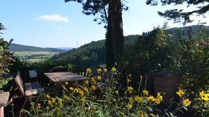 An outdoor seating area with a table and benches, surrounded by yellow flowers and greenery, overlooking a hilly landscape. - Ruhige Wohnung im Sauerland mit Terrasse (Schmallenberg)