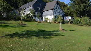 A large two-story house with a steeply pitched roof, surrounded by a well-maintained lawn and dense trees. - Ruhige Wohnung im Sauerland mit Terrasse (Schmallenberg)