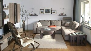 A modern living room with a grey sofa, a coffee table, a rocking chair, and a TV on a wooden stand. - Ruhige Wohnung im Sauerland mit Terrasse (Schmallenberg)