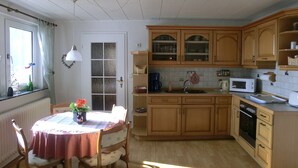 A kitchen with wooden cabinets, a dining table with chairs, a window with curtains, and a radiator. - Ruhige Wohnung im Sauerland mit Terrasse (Schmallenberg)