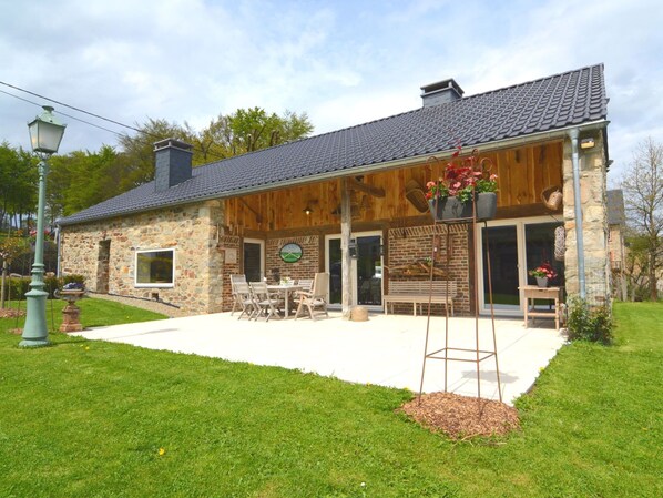 A stone building with a wooden facade, a covered patio with outdoor seating, and a large window. - Beautiful Stone Cottage With Panoramic Views (Waimes)