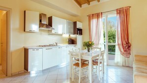 A modern kitchen with white cabinets, a stainless steel range hood, and a dining area with white chairs and a table. - Belvilla by OYO Attractive Residence on Lake Garda (Manerba del Garda)