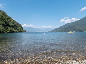A clear lake with visible pebbles and boats, surrounded by mountains and greenery. - Belvilla by OYO Studio Garden Uno (Cannobio)
