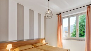 Una cama doble con cabecera de madera, una mesita de noche con lámpara y una ventana con cortinas.