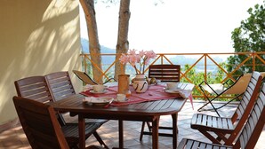 A wooden table with chairs and a vase of pink flowers, set on a balcony with a view of trees and mountains. - Romantic Escape w/ Terrace (Centola)