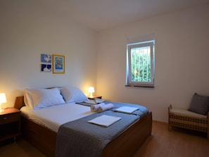 Un dormitorio con una cama, mesitas de noche, un ventanal y una silla.