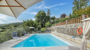 A swimming pool with lounge chairs and an umbrella, surrounded by stone walls and greenery. - Dwelling in Renovated Barn near Birthplace of Michelangelo (Caprese Michelangelo)