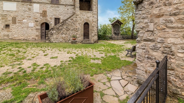 A courtyard with stone buildings, a bench, and a statue. - Dwelling in Renovated Barn near Birthplace of Michelangelo (Caprese Michelangelo)
