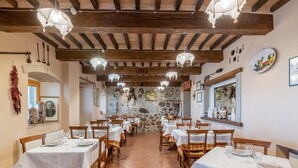 A restaurant with wooden beams, stone walls, and white tablecloths. Tables are set with plates and glasses. - Dwelling in Renovated Barn near Birthplace of Michelangelo (Caprese Michelangelo)