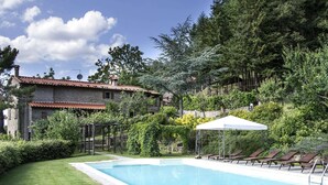 A swimming pool with lounge chairs and a tent, surrounded by a well-maintained garden and a stone building with a tiled roof.